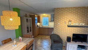 En matplats med ett träbord och stolar, en fåtölj i rotting, en tv på ett stativ och en tegelvägg med en skylt som säger ”välkommen”.