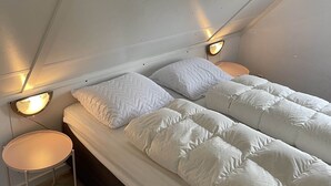 Ett sovrum med en säng, två sänglampor, ett litet runt bord och ett sluttande tak.