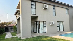 Un edificio moderno de dos pisos con piscina, ventanas amplias y unidad de aire acondicionado.