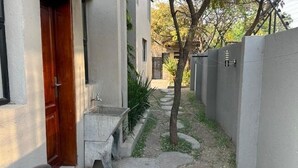 Kapea polku johtaa rakennukseen, jossa on puuovi ja betoninen penkki.