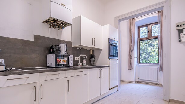 A modern kitchen with white cabinets, a built-in oven, and a window with curtains. - Charming 2BR Apt Vienna Long Stay (Vienna)