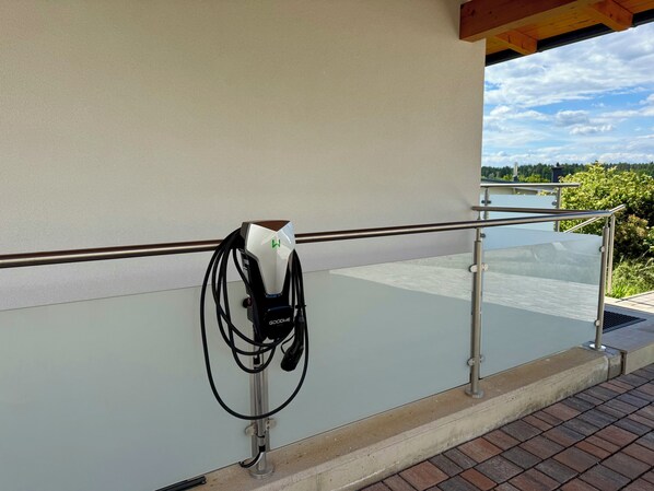 Eine Ladestation für Elektrofahrzeuge mit Glasgeländer und freiem Blick auf Himmel und Grünflächen im Hintergrund.