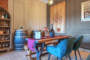 A dining area with a wooden table, two blue chairs, wine glasses, and a wooden barrel.