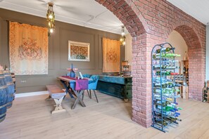 A room with a brick archway, a blue sofa, a wooden table with a purple cloth, and a wine rack.