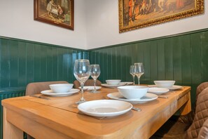 A dining table set with white plates, bowls, and wine glasses, surrounded by green paneled walls and framed artwork. - Pools Cottage 3 Billards Room-Games & Sports Court (Warwickshire)