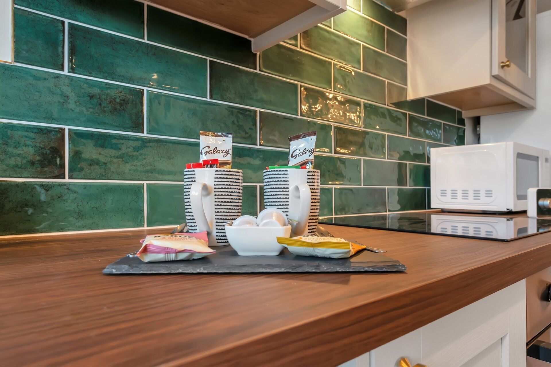 A kitchen counter with two Galaxy-branded coffee cups, a white mug, and a microwave.