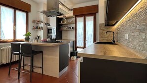 A modern kitchen with a central island, bar stools, a built-in oven, and a stone accent wall. - [VE-Mestre Train Station] Relax&Zen Apartment (Venezia)