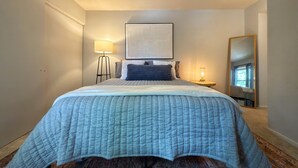 Een slaapkamer met een bed, een bedlampje, een kunstwerk aan de muur en een spiegel.