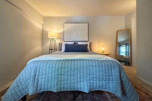 A bedroom with a bed, a bedside lamp, a wall-mounted artwork, and a mirror. - Modern Nambé Condo: Pool, Gym & Gated, Minutes to Downtown SF (Santa Fe)