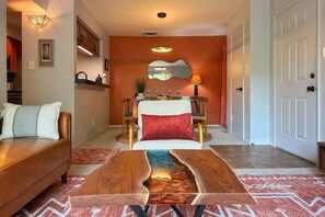 Ein Wohnzimmer mit einer Couch, einem Couchtisch mit Holzmaserung, einem Essbereich mit Tisch für vier Personen und einem Spiegel über dem Tisch.