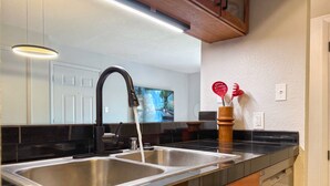 Een moderne keuken met twee roestvrijstalen spoelbakken, een zwart aanrecht, houten kastjes en een houten plafond.