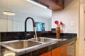 A modern kitchen with two stainless steel sinks, a black countertop, wooden cabinets, and a wooden ceiling. - Modern Nambé Condo: Pool, Gym & Gated, Minutes to Downtown SF (Santa Fe)