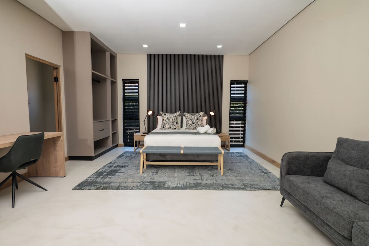 A modern bedroom with a bed, bedside tables, a desk, a chair, and a sofa.