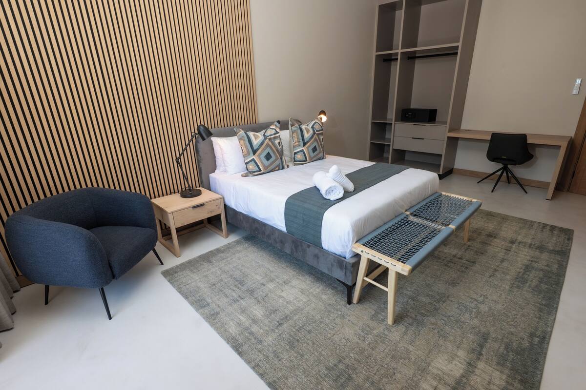 A modern bedroom with a bed, bedside tables, a chair, and a desk.
