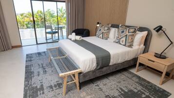 A modern bedroom with a large bed, a small desk, and a view of palm trees through the balcony doors.