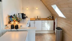 Een kleine keuken met een houten plafond, dakraam en witte kastjes.