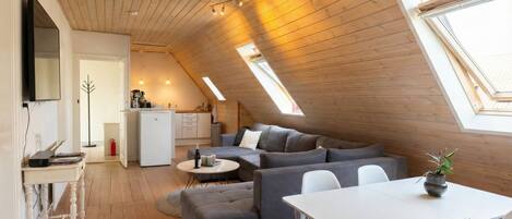 A modern loft with a sloped ceiling, a dining area, a sofa set, and a kitchen.