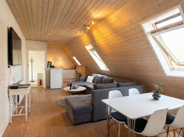 A modern loft with a sloped ceiling, a dining area, a sofa set, and a kitchen.