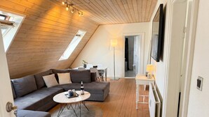 Een moderne loft slaapkamer met een schuine plafond, houten vloer, een hoekbank, een ronde salontafel en een aan de muur bevestigde televisie.