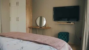 Un dormitorio con cama, armario, espejo, televisor y una pequeña silla verde.