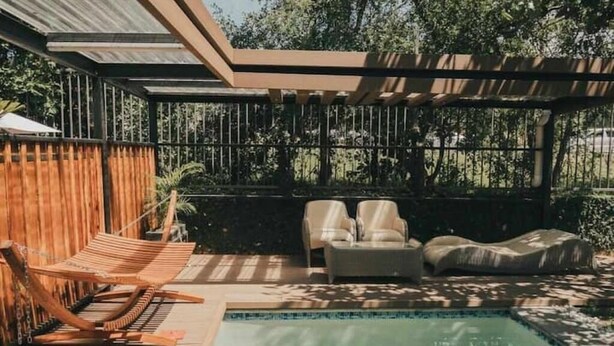 Zona junto a la piscina con muelle de madera, una silla de descanso, un sofá y una pérgola.