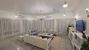 A spacious living room with a large sofa, two armchairs, a coffee table, and a TV.