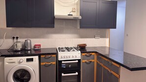 A compact kitchen with a washing machine, a gas stove, and cabinets. - Charming Guest Room in Morden with Modern Amenities (Morden)