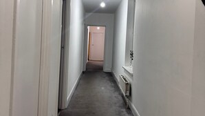 A narrow hallway with white walls and a grey carpet. There are doors on both sides and a radiator on the right wall. - Charming Guest Room in Morden with Modern Amenities (Morden)