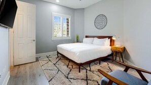 A bedroom with a bed, a ceiling fan, a nightstand, a lamp, a wall art piece, and a window with blinds. - Terra Sol: Pool, Spa & Lakefront Serenity (Indio)