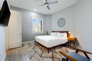 A bedroom with a bed, a ceiling fan, a nightstand, a lamp, a wall art piece, and a window with blinds. - Terra Sol: Pool, Spa & Lakefront Serenity (Indio)