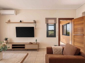 Ein Wohnzimmer mit einem Flachbildfernseher, einem Holzkonsolentisch, einem braunen Sofa und einer Glasschiebetür, die zu einem Außenbereich führt.
