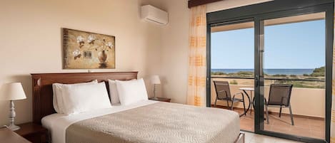 Ein Hotelzimmer mit Bett, einem Bild, einer Klimaanlage, einem Balkon mit Stühlen und Blick auf den Strand.