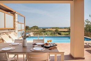 Ein Esstisch, gedeckt mit Tellern, Besteck und einer Blumenvase, mit Blick auf einen Swimmingpool und eine schöne Landschaft.