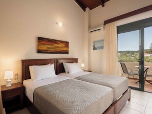 Ein Hotelzimmer mit zwei Betten, einem Gemälde, einer Klimaanlage, Blick ins Freie und einem Balkon mit Sitzgelegenheiten.