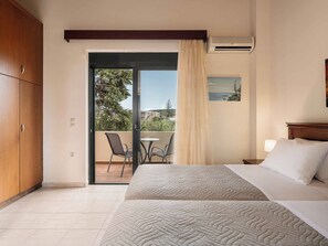 Ein Hotelzimmer mit Bett, Balkon mit Stühlen, einem Holzschrank und einer Klimaanlage.