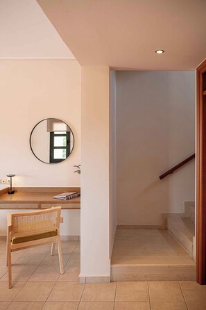 Ein Zimmer mit einem Holztisch, einem Stuhl, einem runden Spiegel und einer Treppe, die in ein Obergeschoss führt.