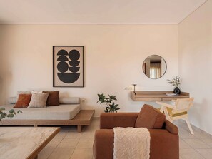 A living room with a sofa, a coffee table, a brown couch, a round mirror, a wooden console table, and a framed abstract artwork. - Corali Villas West-Seaview, 2 Pools, 450m to Beach (Chania)