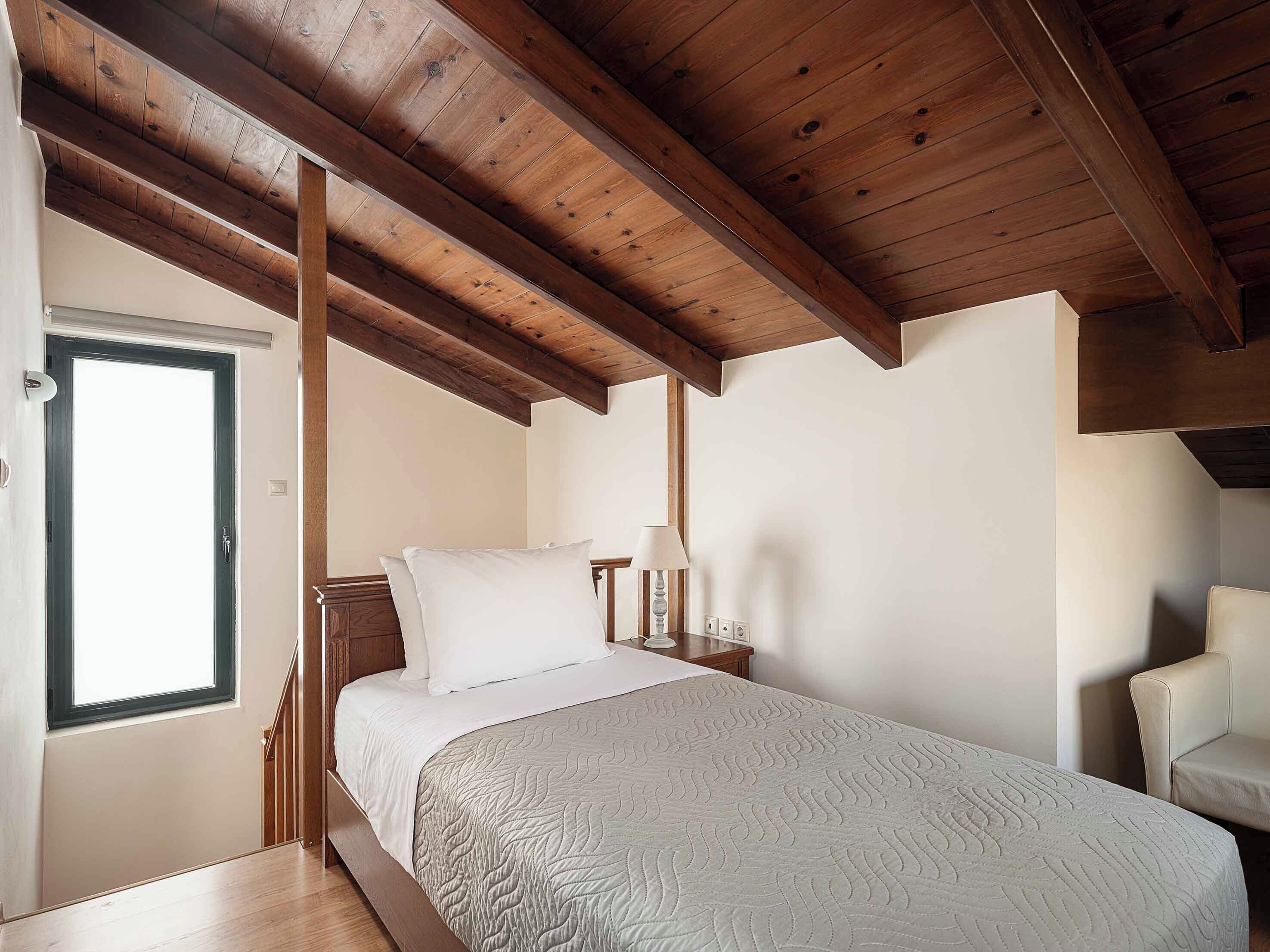 Une chambre avec un plafond en bois, un lit avec une literie blanche, une table de chevet avec une lampe et une chaise.