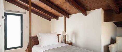 Un dormitorio con techo de madera, una cama con ropa de cama blanca, una mesita de noche con lámpara y una silla.