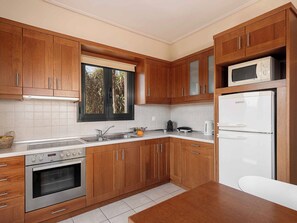 A modern kitchen with wooden cabinets, a built-in microwave, a stainless steel oven, and a window with blinds. - Corali Villas Complex-Seaview,4 Pools,450 to Beach (Chania)