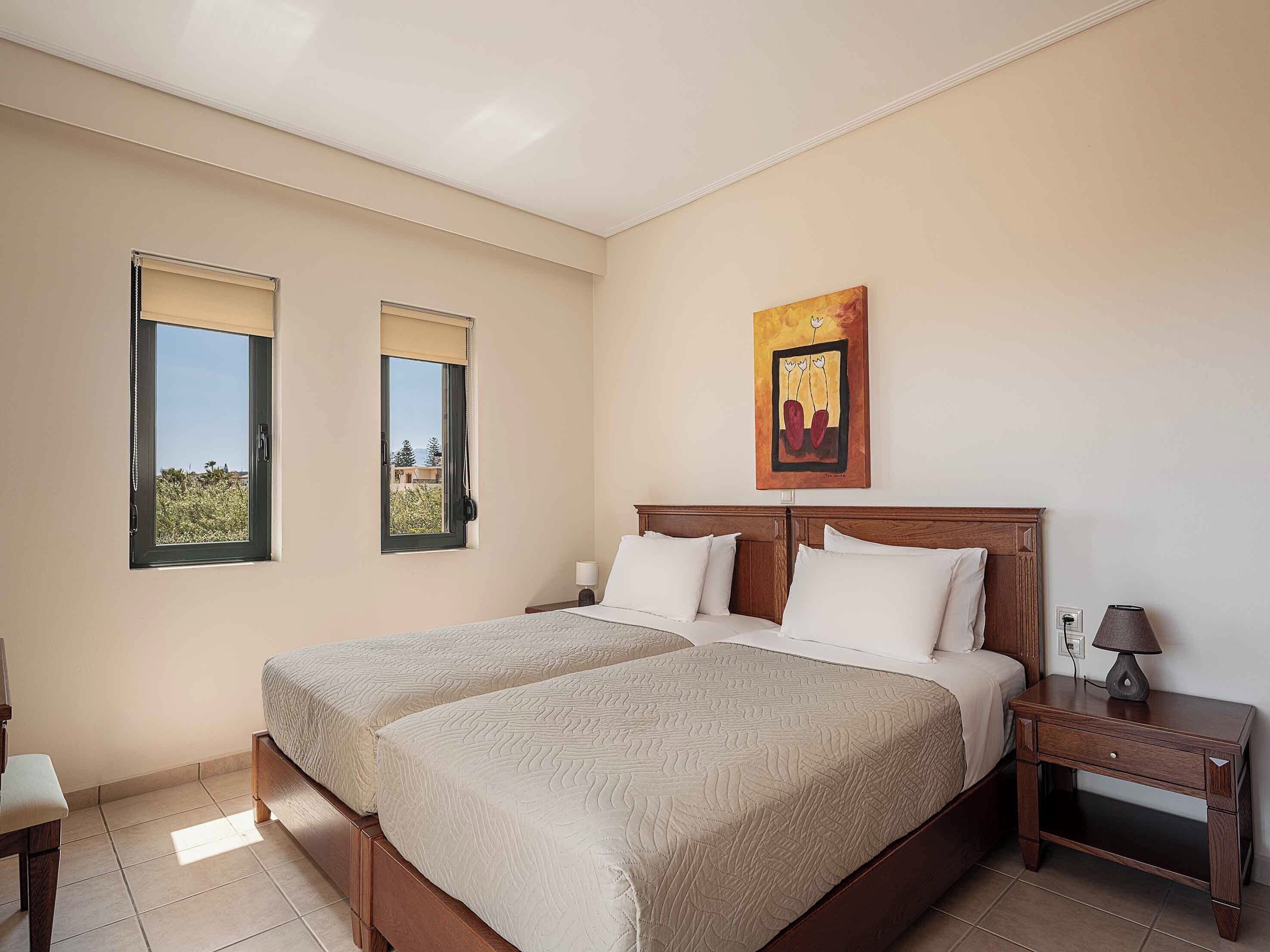 A bedroom with two beds, a nightstand, a lamp, and a painting on the wall.