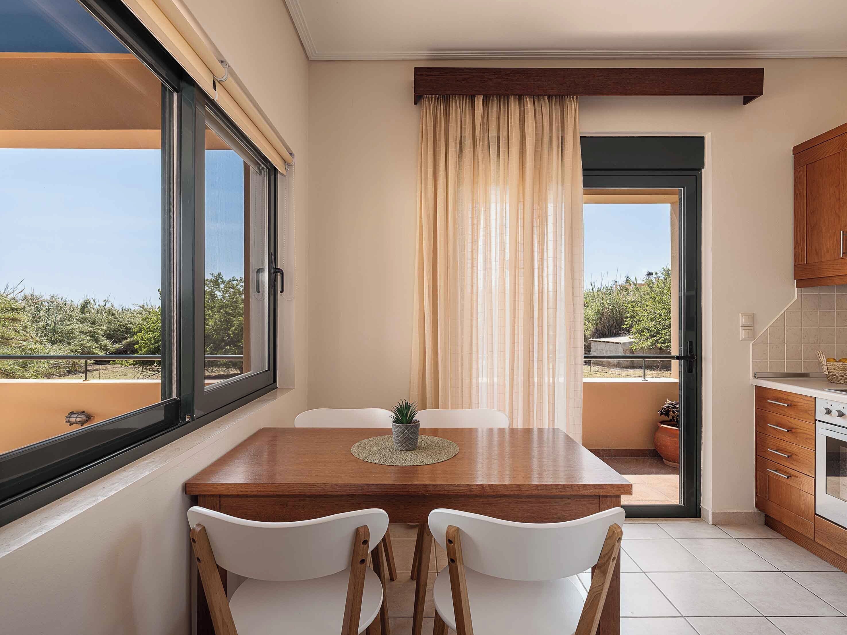 Uma área de refeições com mesa e cadeiras, vista pela janela e uma cozinha com armários.