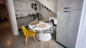 Een moderne keuken met grijze kastjes, een eettafel met twee stoelen en een airconditioning unit boven de toonbank.