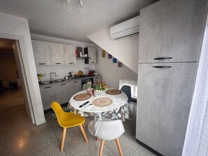 Een moderne keuken met grijze kastjes, een eettafel met twee stoelen en een airconditioning unit boven de toonbank.