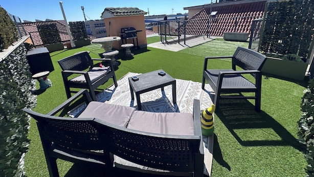 A rooftop patio with outdoor furniture, a barbecue grill, and a small seating area.