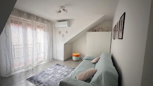 Een kamer met een schuine kap, een bed met kussens, een vloerkleed, een kledingkast en een klein krukje.
