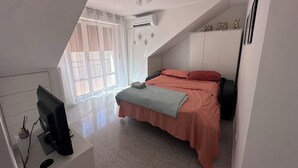 A bedroom with a bed, a desk with a computer, a window with curtains, and a ceiling fan.