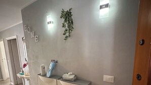 Een hal met een grijze muur, een bord met de tekst 'HOME', een kamerplant en een console tafel met decoratieve objecten.