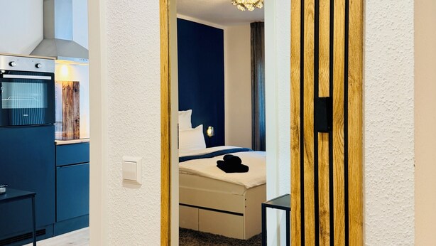 Ein Hotelzimmer mit einem großen Spiegel, einem Bett, einem Nachttisch und Blick auf den Küchenbereich.