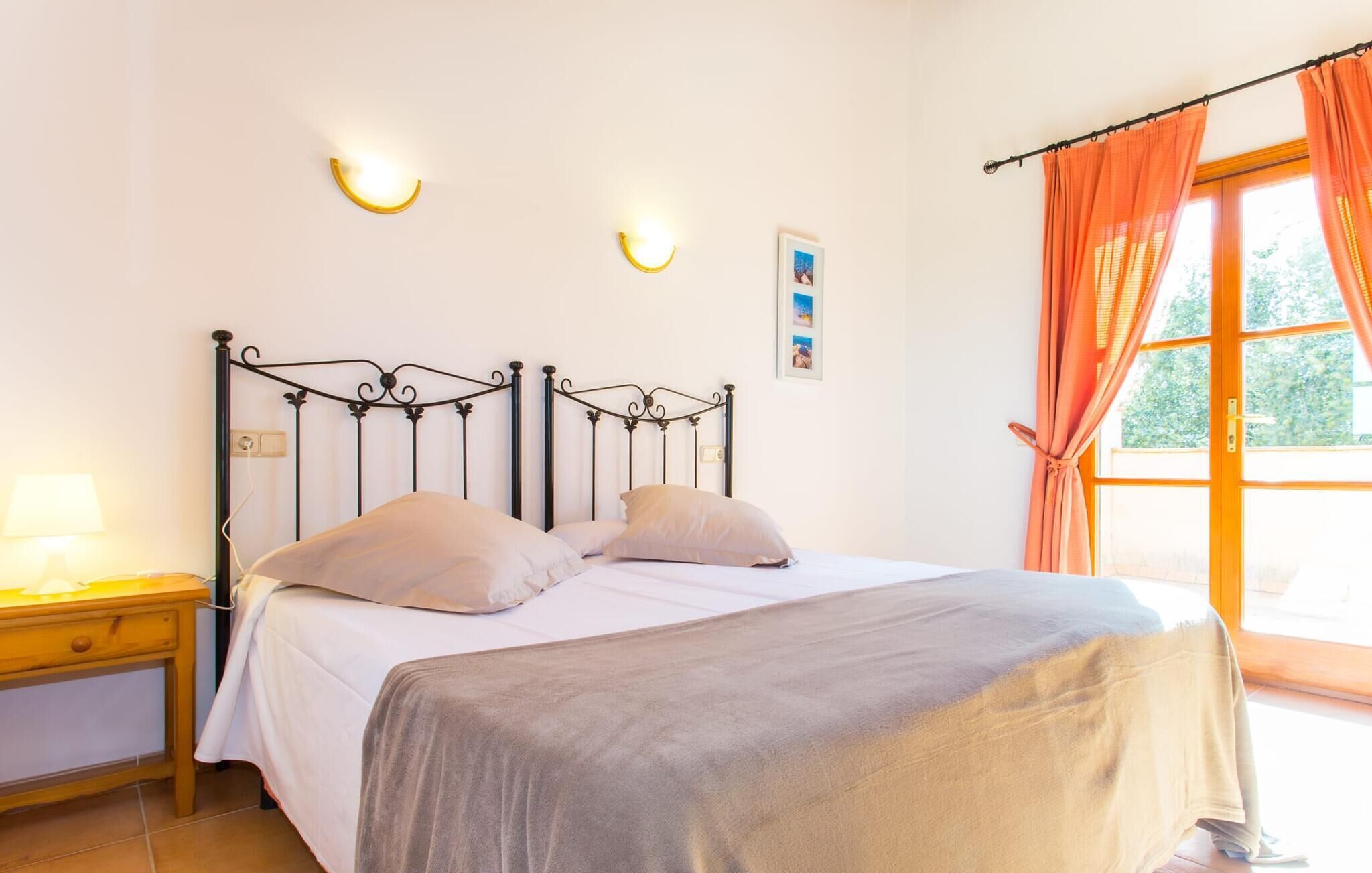 Een slaapkamer met een bed, nachtkastje, lamp en een raam met gordijnen.